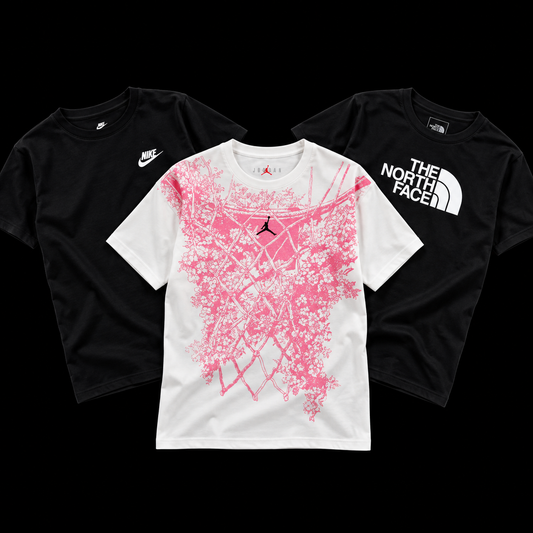 Three graphic t-shirts arranged on a black background: a black Nike t-shirt on the left, a black The North Face t-shirt on the right, and a white t-shirt in the center featuring a large pink basketball net graphic with a black Jordan logo.